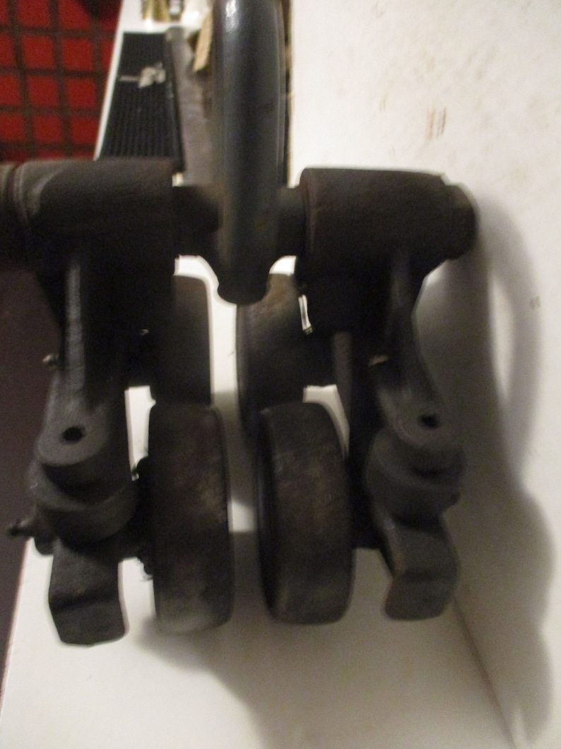 May include: A close-up of a vintage, dark gray metal tool. The tool has a handle and several rounded components, including what appear to be wheels. The object is set against a white surface.