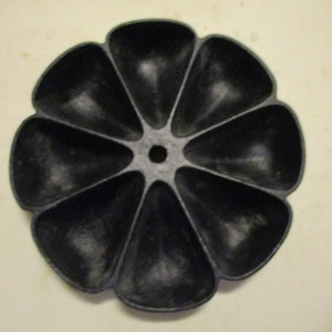 May include: Black cast iron divided dish with eight sections and a central hole. The dish is round and has a scalloped edge.
