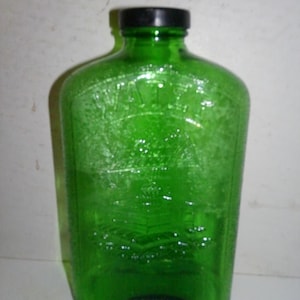 May include: A green glass bottle with a black plastic lid. The bottle has a label that says "Whiskey" and "100 Proof".