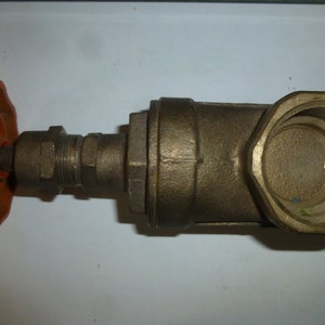 May include: A bronze gate valve with a red, spoked handwheel. The valve body is a brass color with threaded connections and a hexagonal end. The handwheel is painted red and shows signs of wear.