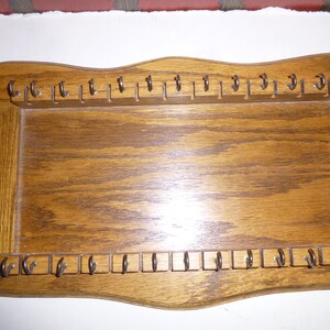 May include: A wooden key holder with a wavy top and bottom edge. It has two rows of hooks, each with 15 hooks. The key holder is made of light brown wood with a natural wood grain.