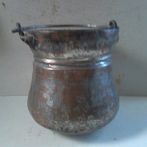 May include: A vintage copper pot with a worn finish and two handles. The pot has a rounded bottom and a wide opening.