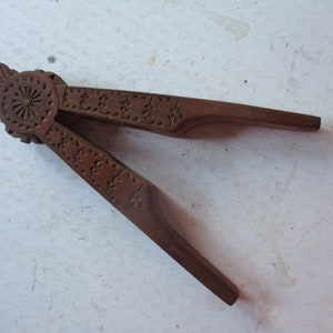 May include: A vintage wooden nutcracker with intricate star and floral carvings. The dark brown tool features a lever design for cracking nuts. The handle has a decorative carved pattern.