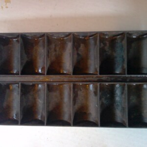 May include: A vintage cast iron muffin tin with 12 individual molds. The molds are shaped like small, rounded cups.
