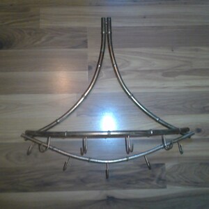 May include: A gold-toned metal rack with multiple hooks, designed for hanging items. The rack is curved and has a triangular shape.