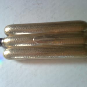 May include: A gold-colored, three-sectioned, hinged flask with a black cap. The flask has a textured, hammered finish.