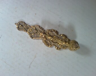 May include: A gold-toned metal hook with an ornate design. The hook has a decorative scrollwork pattern and a rounded end.