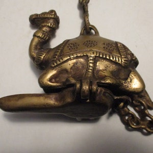 May include: A vintage brass camel-shaped oil lamp with intricate details. The lamp features a hinged lid, a spout, and a decorative chain. The camel is adorned with etched patterns, showcasing a classic design.