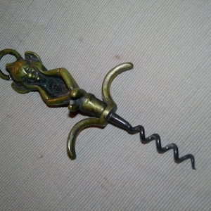 May include: Antique brass-toned corkscrew with a detailed devil figure on top. The corkscrew features a spiral worm and curved handles for leverage. A unique barware accessory.