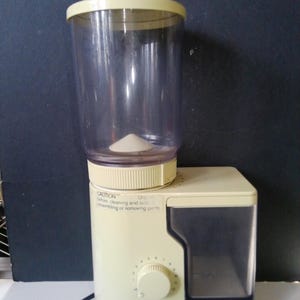 May include: A white ceramic mug with a black handle and the text "But First, Coffee" in a black, handwritten-style font. The mug is on a white surface.