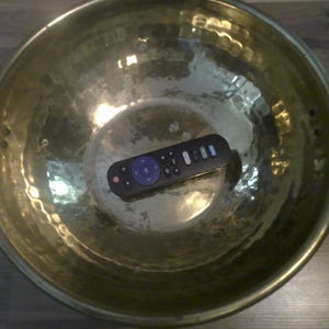 May include: A gold-colored metal bowl with a hammered texture and a black remote control inside.