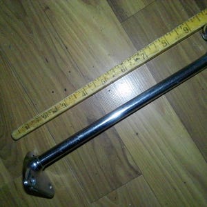 May include: A chrome-plated metal bar with a curved end and a mounting plate. A wooden ruler is placed diagonally across the bar. The bar appears to be approximately 10 inches long.