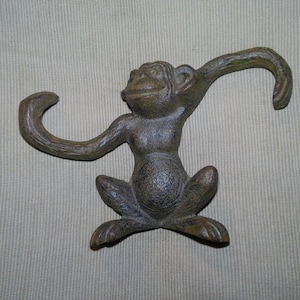 May include: A bronze-colored monkey figurine with outstretched arms and legs. The monkey is in a seated position with its arms curved upwards. The figurine has a textured surface and is likely made of metal.