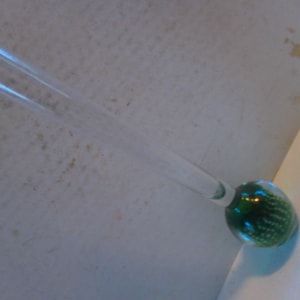 May include: A tall, clear glass vase with a green, textured, spherical base.