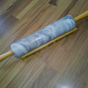 May include: A gray marble rolling pin with a wooden handle and a wooden stand with the text "Gourmet Kitchen" printed on it.