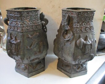 May include: Two antique bronze urns with intricate carvings and decorative handles. The urns are hexagonal in shape and feature a variety of designs, including birds, flowers, and geometric patterns.