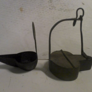 May include: Two antique oil lamps made of metal. One lamp has a long spout and a handle. The other lamp has a round body and a handle.