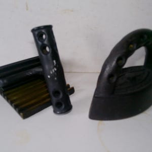 May include: A black cast iron vintage iron with a handle and a black metal ironing board with a wooden handle.