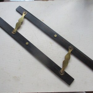May include: Two black wooden rulers with brass handles and fasteners. The rulers are joined together at the handles.