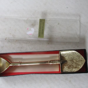 May include: Gold-colored bottle opener and ice crusher shaped like a shovel in a red and black box. The box has the text "Bottle Opener Ice Crusher & Scoop" on it.