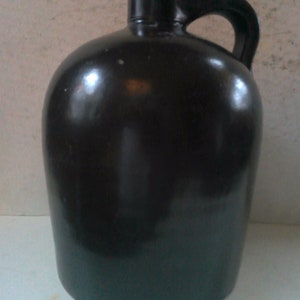 May include: A black glazed ceramic jug with a rounded body and a single handle. The jug has a smooth, glossy finish.