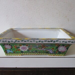 May include: A rectangular ceramic planter with a green, yellow, and white floral design. The planter has a white interior and a yellow rim.