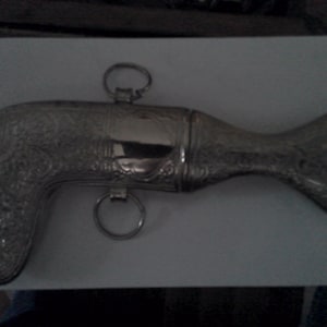 May include: A silver-colored, ornate, decorative dagger with a curved handle and a long, thin blade. The dagger has intricate floral designs etched into the metal.