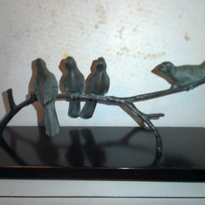May include: A bronze sculpture of four birds perched on a branch. The birds are all facing the same direction, and the branch is attached to a black wooden base.