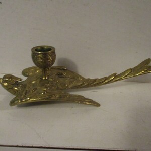 K&ouml;nnte beinhalten: Ein Messing-Kerzenhalter in Form eines Vogels im Flug. Der Vogel hat ausgebreitete Fl&uuml;gel und ein detailliertes Federdesign. Der Kerzenhalter ist eine kleine Tasse, geeignet f&uuml;r eine einzelne Kerze. Das Design ist vintage und dekorativ.