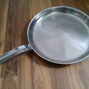 May include: A stainless steel frying pan with a long handle. The pan is empty and clean.
