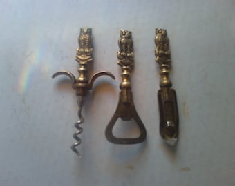 May include: Set of three gold-toned metal bottle openers with owl designs. The openers include a corkscrew, a bottle opener, and a bottle cap opener.