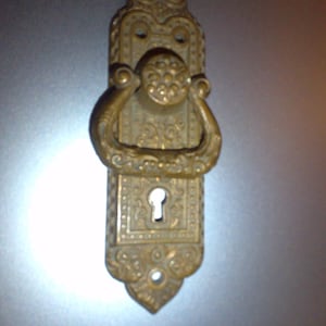 May include: Ornate brass door handle with a keyhole and a decorative ring pull. The handle has a detailed floral design.