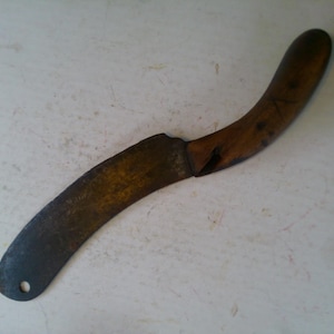 May include: A curved knife with a wooden handle and a dark, aged blade. The blade has a small hole near the tip. The knife appears to be vintage or antique, with signs of wear and use.