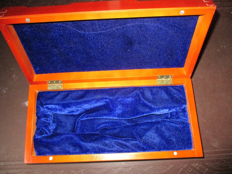 Pu&ograve; includere: Scatola di legno aperta con un esterno marrone rossiccio intenso e un interno in velluto blu vibrante. La scatola &egrave; rettangolare con cerniere in ottone e una fodera morbida e soffice, che suggerisce un astuccio per gioielli o altri oggetti di valore.