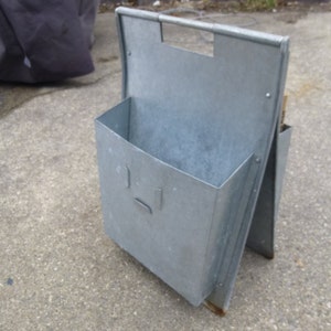 May include: A silver metal magazine rack with a rectangular opening. The rack is folded to create a stand.