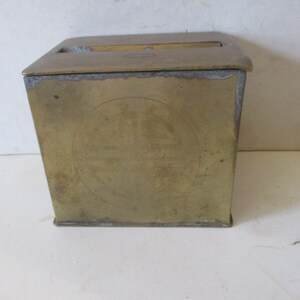 May include: A brass box with a hinged lid and a circular design on the front. The box is closed and appears to be antique.