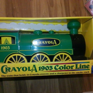 May include: A green toy train with yellow wheels and the text "CRAYOLA 1903 Color Line" on the box. The train holds 24 crayons and a sharpener. The train is in a yellow box.