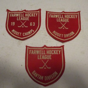 May include: Three red felt patches with white lettering. The patches are shaped like shields and have the text "Farwell Hockey League" with a hockey stick graphic. The top two patches say "Midget" and the bottom patch says "Bantam".