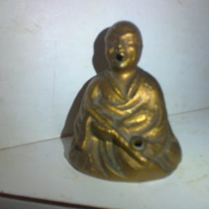 May include: A gold-colored figurine of a person sitting with their hands clasped in front of them. The figurine is wearing a robe and has a serene expression on their face.