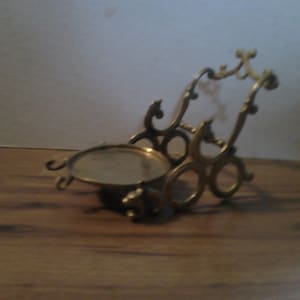 May include: A brass decorative stand with a round, mirrored top and intricate scrollwork design.