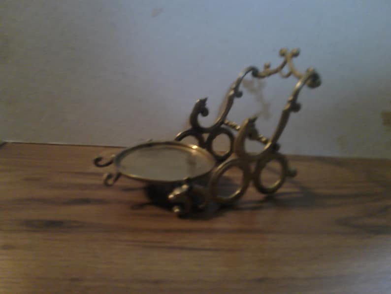 May include: A brass decorative stand with a round, mirrored top and intricate scrollwork design.