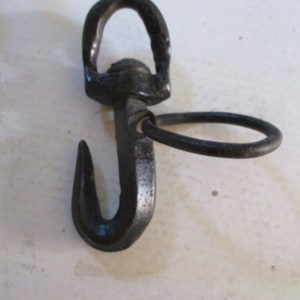 May include: Black metal hook with a ring attached to the top. The hook is curved and has a pointed end.