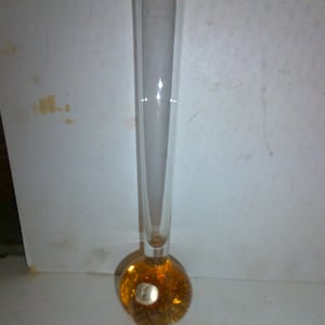 May include: A clear glass vase with a long, slender neck and a rounded, amber-colored base. The base has a textured, bubble-like appearance. The vase is designed to hold flowers and other decorative items.