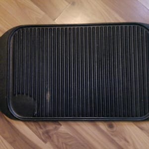 May include: Black rectangular cast iron grill pan with a ridged cooking surface. The pan has rounded corners and a small, raised handle on one side. The grill pan is designed for stovetop cooking and grilling.