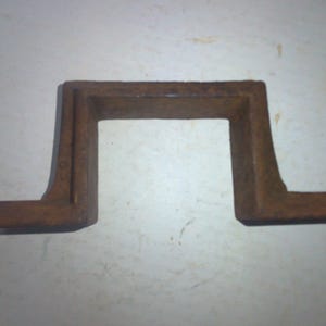 May include: A rusty metal U-shaped bracket with a rectangular opening in the center.