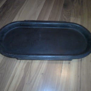 May include: A black cast iron oval griddle with two handles.