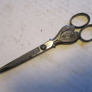 May include: Antique silver-plated scissors with ornate handles featuring a heart-shaped design and engraved details. The blades are sharp and the scissors are in good condition.