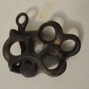 May include: A cast iron antique pulley with multiple loops and a small knob. The pulley is dark brown and has a worn, rustic look.