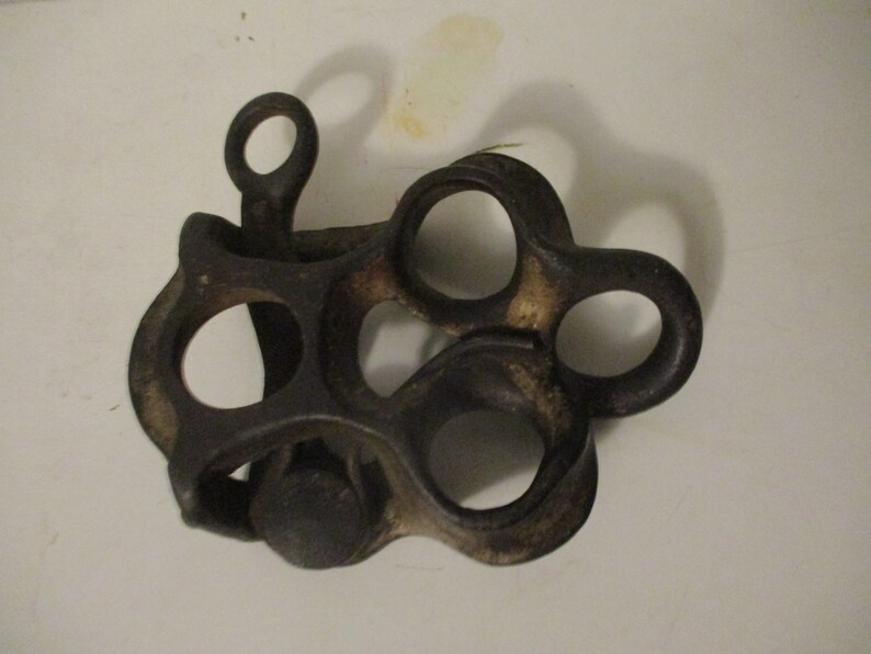 May include: A cast iron antique pulley with multiple loops and a small knob. The pulley is dark brown and has a worn, rustic look.