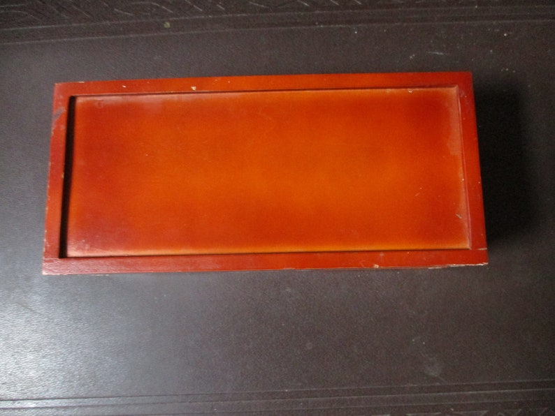 Pu&ograve; includere: Un vassoio rettangolare in legno con finitura marrone-rossastra lucida. Il vassoio ha un bordo rialzato e una superficie liscia e lucida. La venatura del legno &egrave; visibile, aggiungendo alla sua estetica naturale. Il vassoio &egrave; vuoto e poggia su una superficie scura.